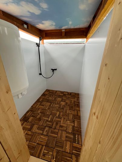 Une salle de douche moderne avec un sol en bois et une douche. Les murs sont clairs et le ciel est représenté au plafond.