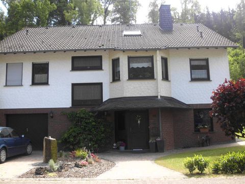 Ein zweistöckiges Wohnhaus mit einem gemischten Farbschema aus Weiß und Braun. Vor dem Haus befinden sich ein kleiner Garten und ein Auto in der Einfahrt.