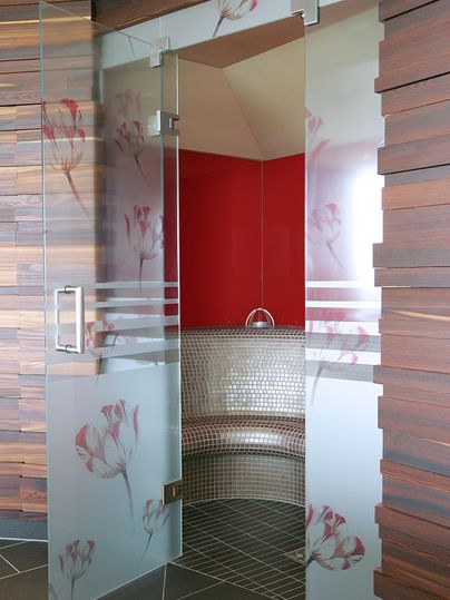 A modern wellness oasis with a glass door and a stylish seating area made of mosaic. The walls are decorated with warm wooden surfaces and a red accent.