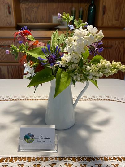 Un beau bouquet de fleurs dans une théière blanche sur une table. À côté se trouve une petite carte d'information.